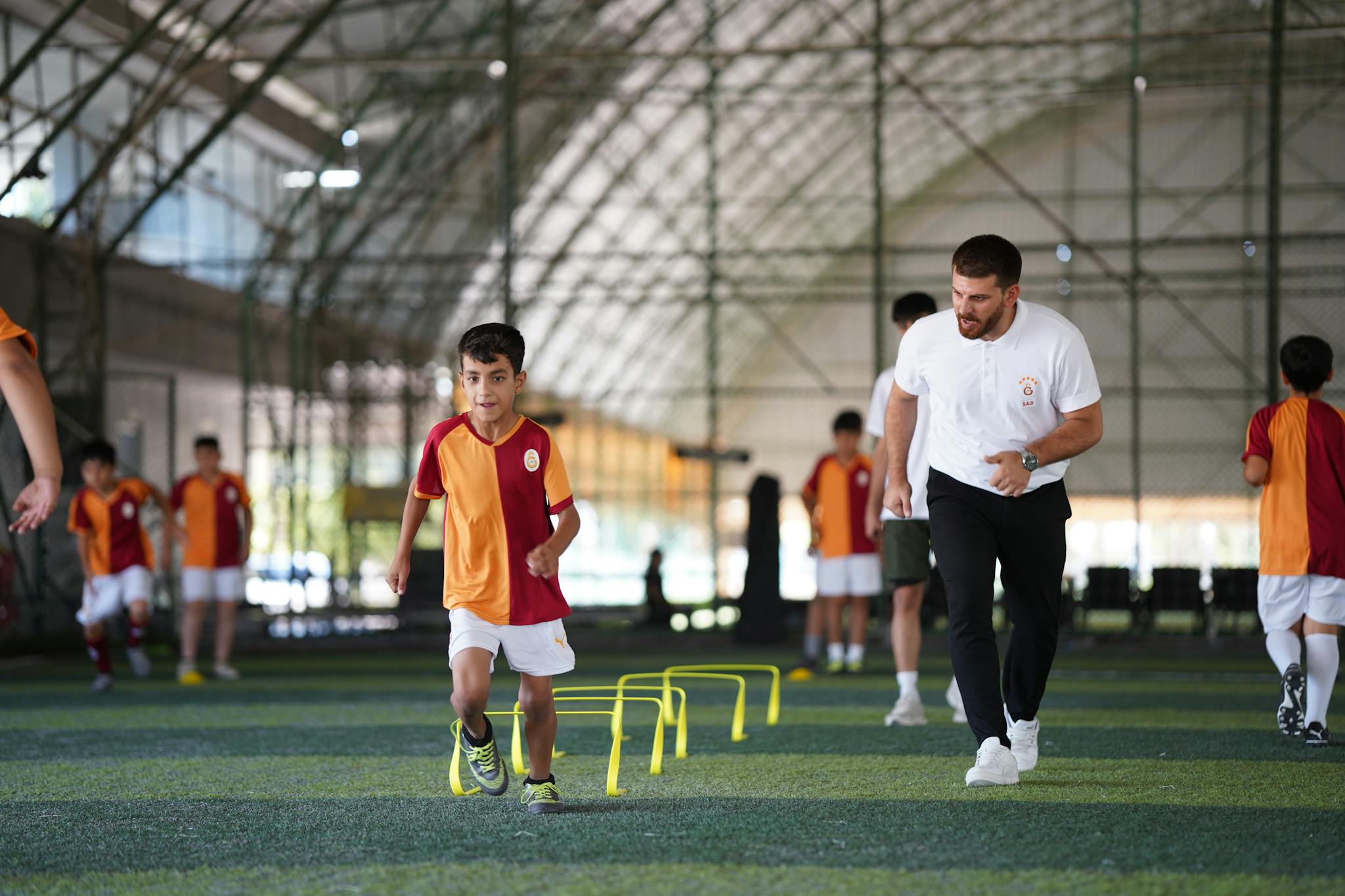 Energetic indoor soccer training with kids and coach, focusing on agility and teamwork.