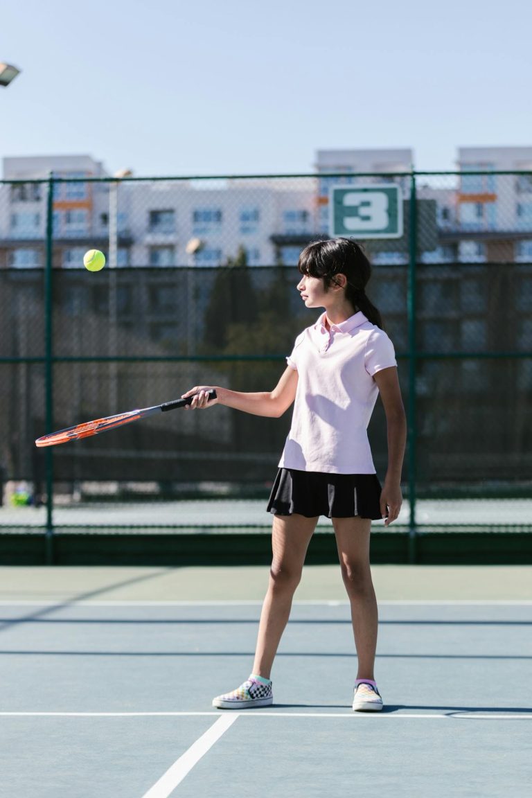 Teen girl practicing tennis with racket and ball on a sunny outdoor court.